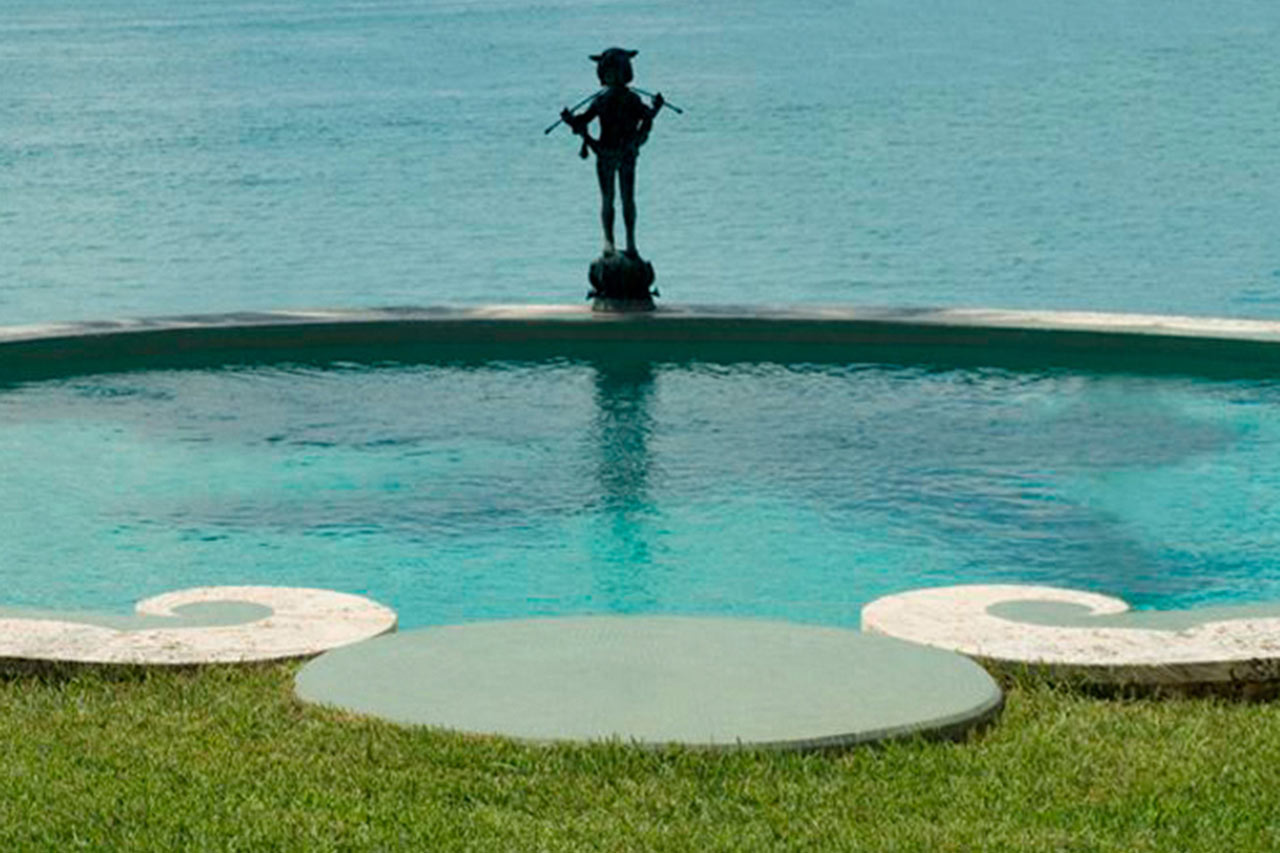 pool with pan statue of an Oval stone & mosaic pool in Miami Beach designed by Maria de la Guardia & Teofilo Victoria of DLGV Architects & Urbanists
